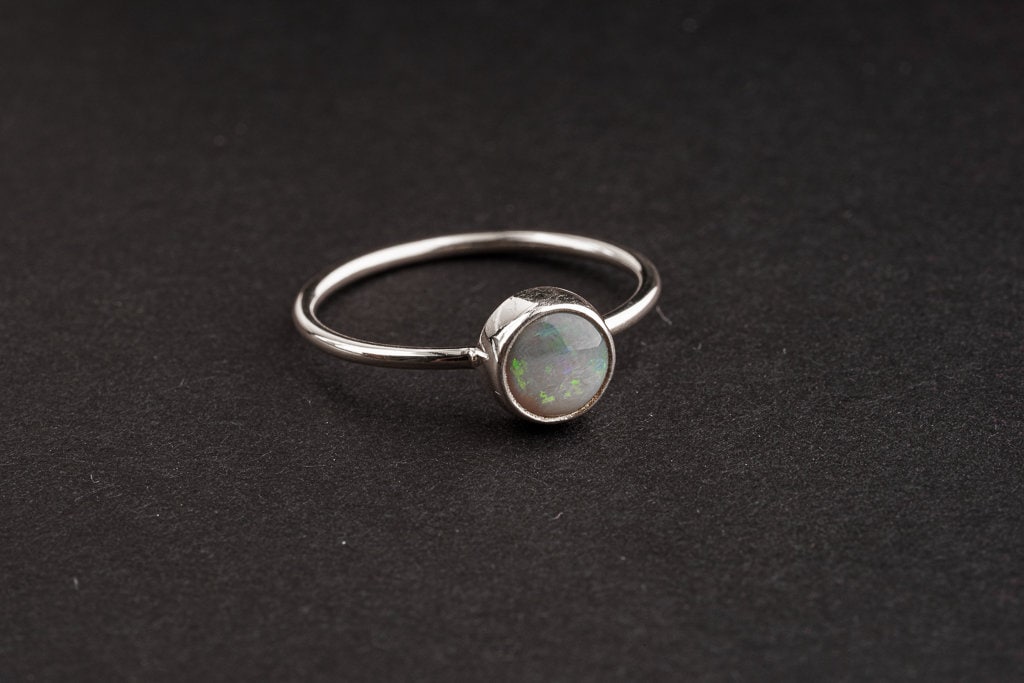 Handmade 925 sterling silver Lightning Ridge Black Opal ring shown on a dark background, with rough opal and fine silver band.