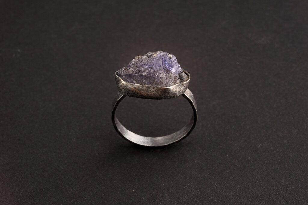 Raw Tanzanite Silver Ring shown on black background with upright blue-violet raw gemstone and fine silver band.