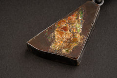Close-up of Ammolite fossil pendant showing red, gold, green, and orange iridescent colour play in textured silver bezel.