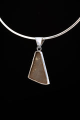 Ammolite fossil pendant on black background with brushed sterling silver setting and triangular freeform shape.