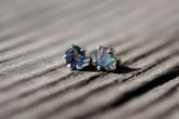 Handmade 925 sterling silver Australian Sapphire stud earrings shown on wood, with creek tumbled blue gemstones and 6-claw settings.