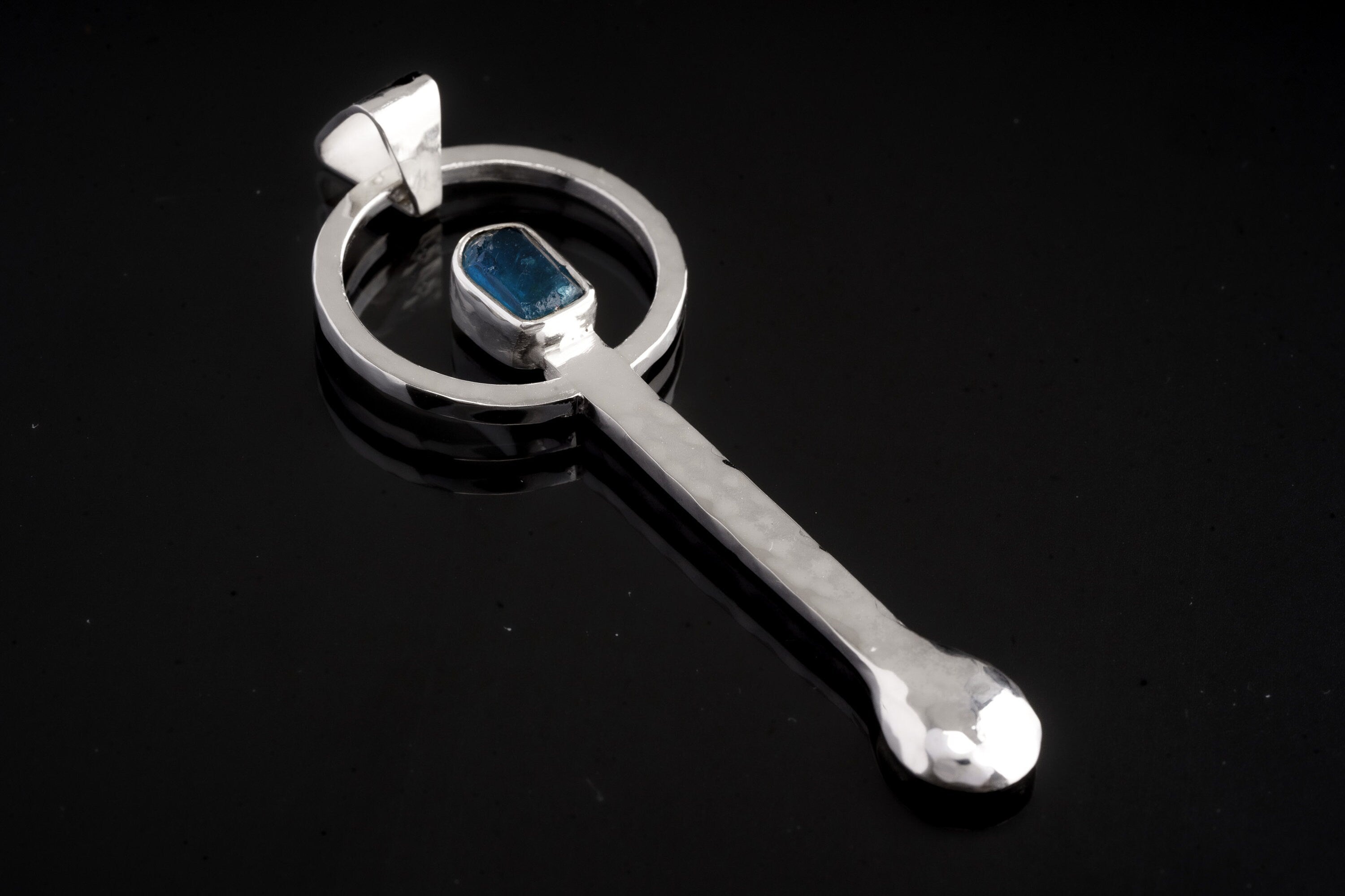 Blue Apatite sterling silver hammered spoon pendant shown on dark background with vivid blue gemstone setting.