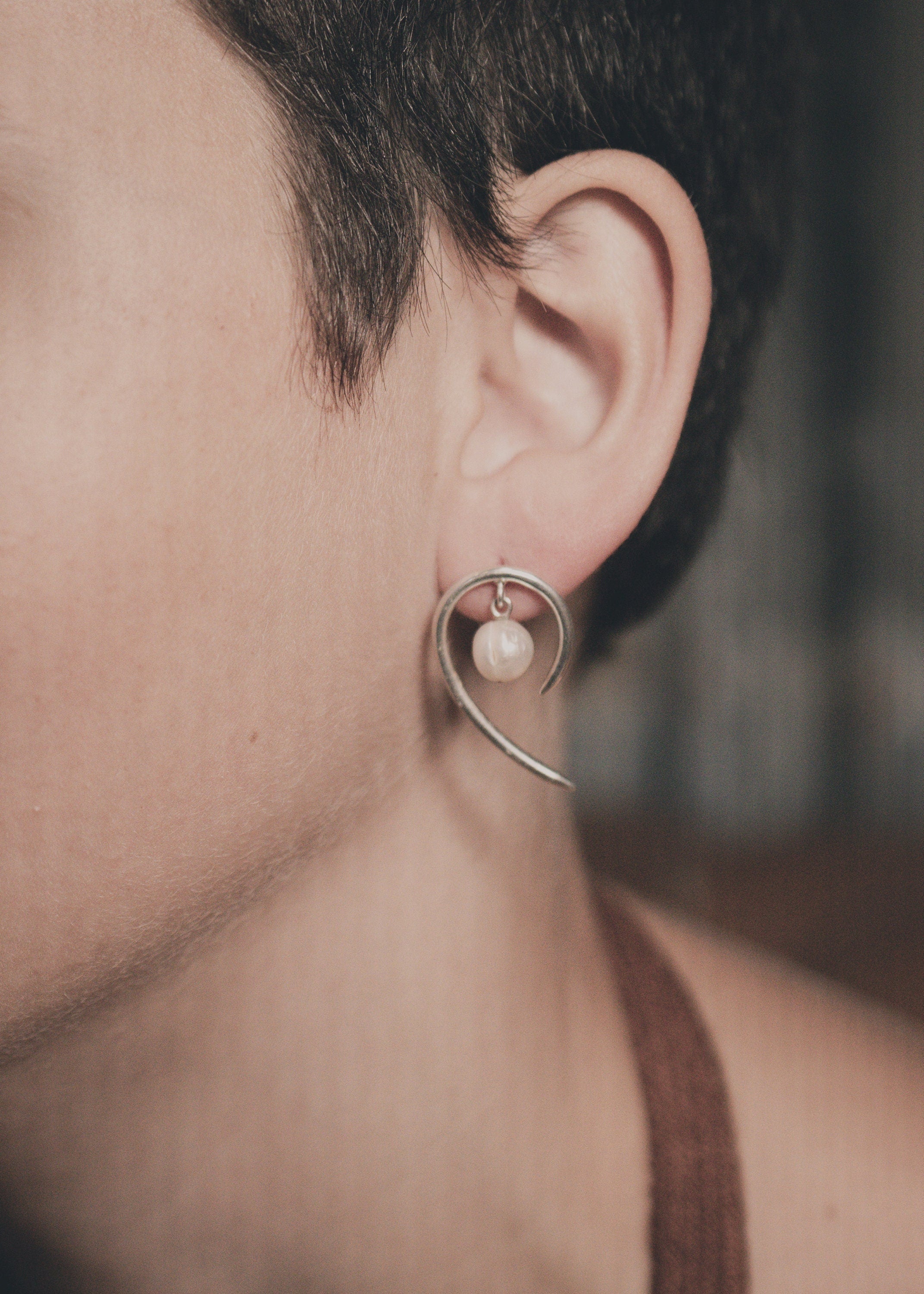 Handmade 925 sterling silver Pearl swirl earrings shown worn on the ear, with natural Pearl and curved silver drop design.