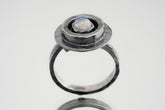 Blue Moonstone Ring shown on white background with oxidized sterling silver setting and oval blue-white cabochon.