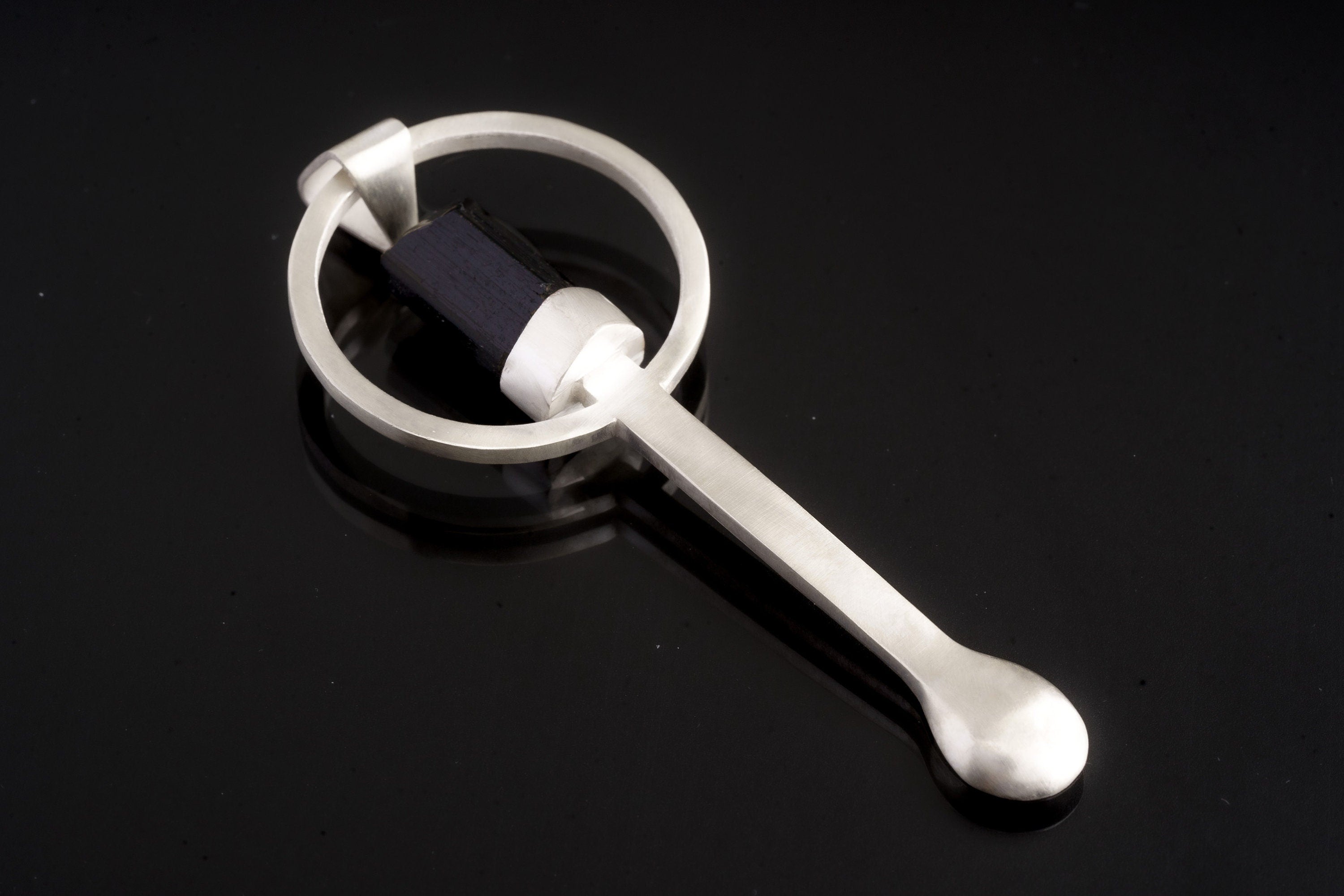 Black Tourmaline sterling silver hammered spoon pendant shown on dark background with sculptural silver form.