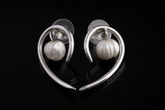 Pearl sterling silver earrings shown on a dark background, with sculptural swirl shape and soft natural Pearl lustre.