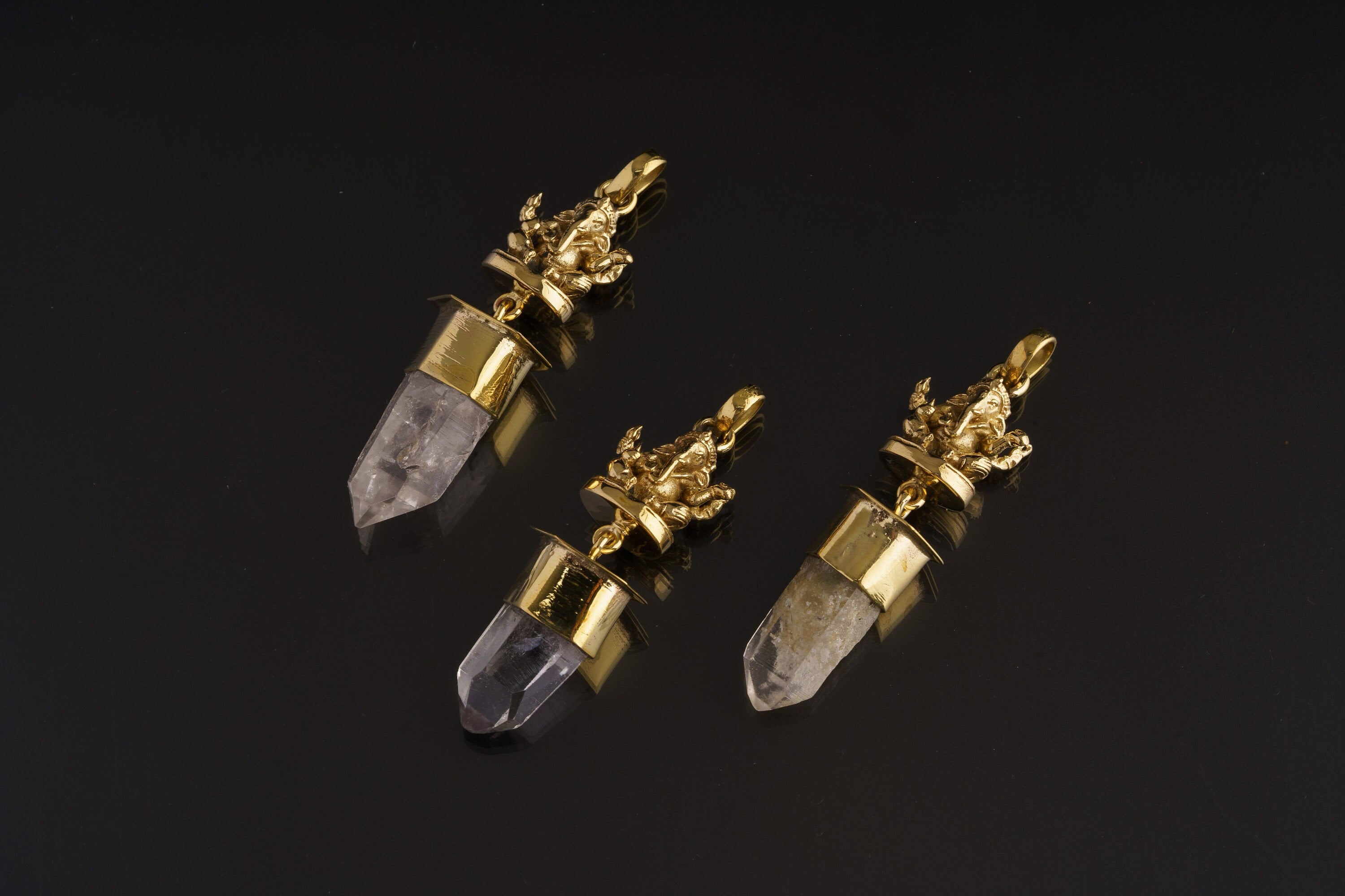 Meditating Ganesha Clear Quartz talisman pendant shown on black background with golden brass figure and crystal point.