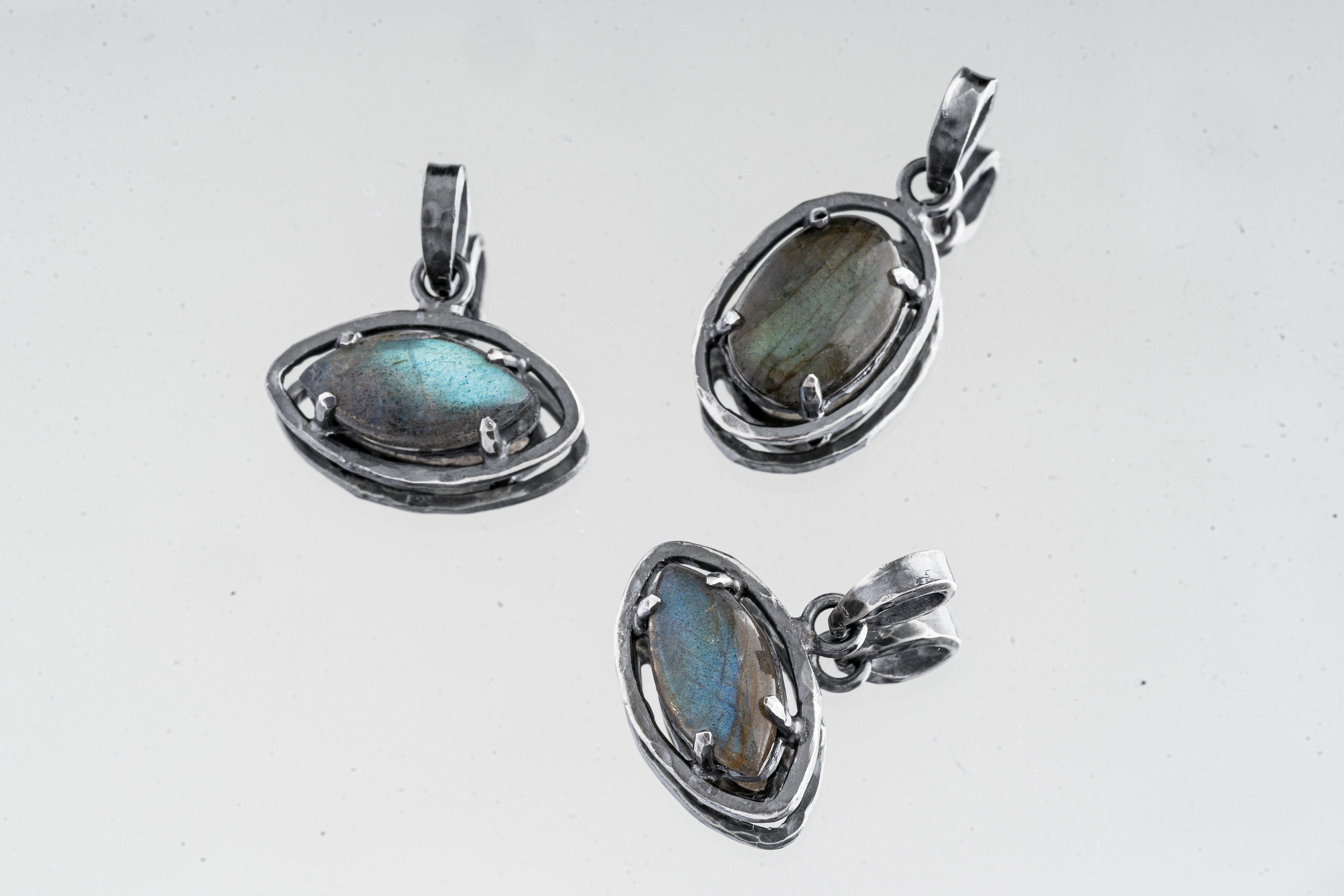 Collection of oxidized 925 sterling silver Madagascan Labradorite claw pendants with shifting blue-green flash on a light background.