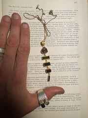 Tourmaline Tapestry pendant shown held against a book, featuring Black Opal, Watermelon Tourmaline, Green Tourmaline, Dravite, and Indicolite.