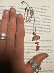 Statement gemstone pendant shown held against a book, featuring pink Tourmaline, Ruby, Black Opal, and 18k gold-plated silver.