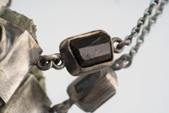 Close-up of dark faceted Garnet accent beside the sterling silver chain on the Verdant Quartz Relic Necklace.