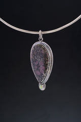Close-up of Ruby in Black Matrix Ethiopian Opal pendant showing opal accent and textured sterling silver sun-ray detail.