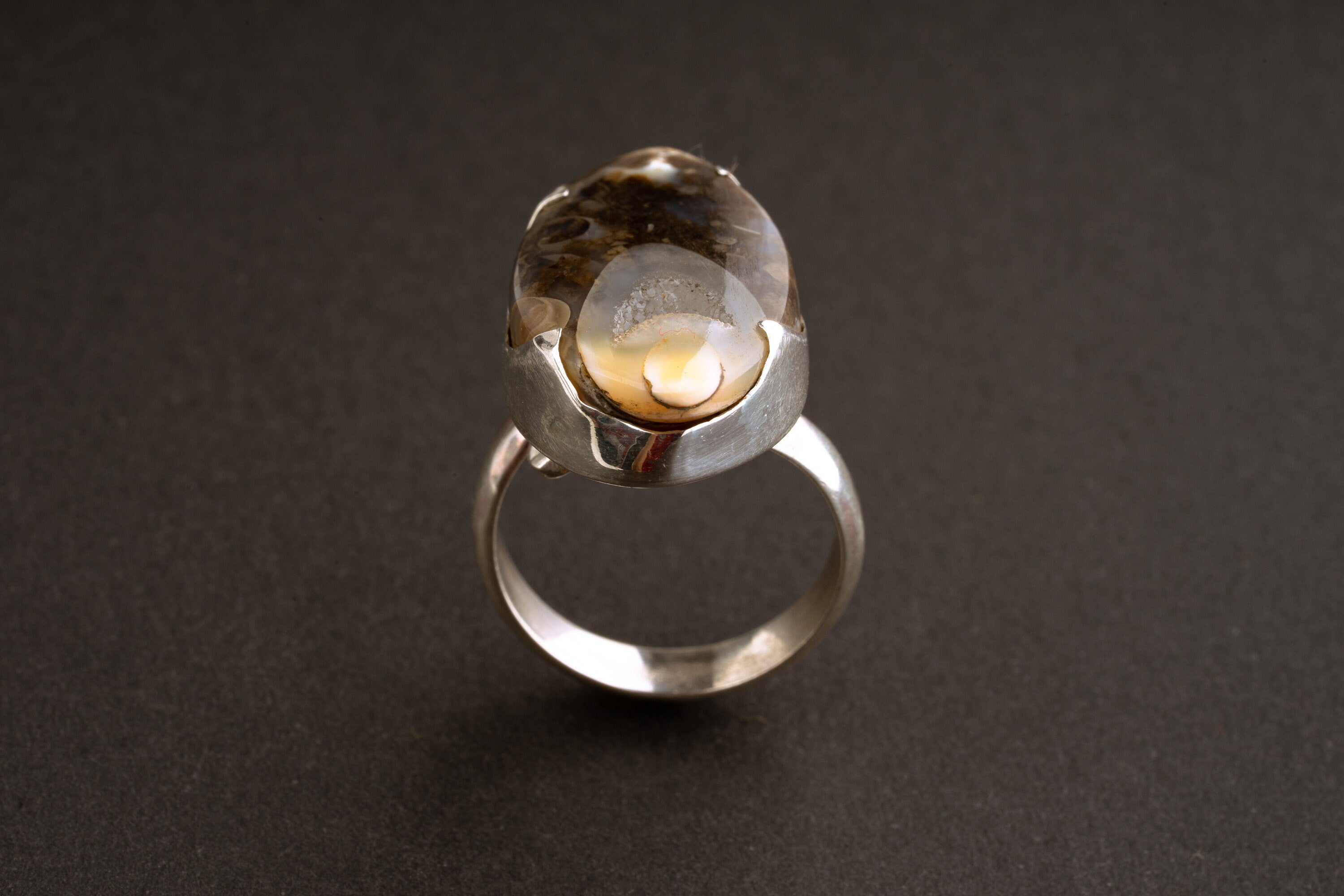 Ancient crystalized shell ring shown on dark background with adjustable sterling silver statement setting.