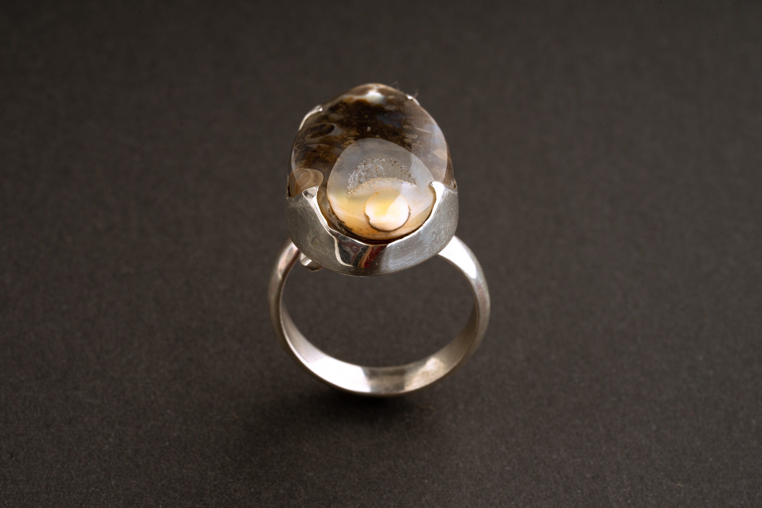 Ancient crystalized shell ring shown on dark background with adjustable sterling silver statement setting.