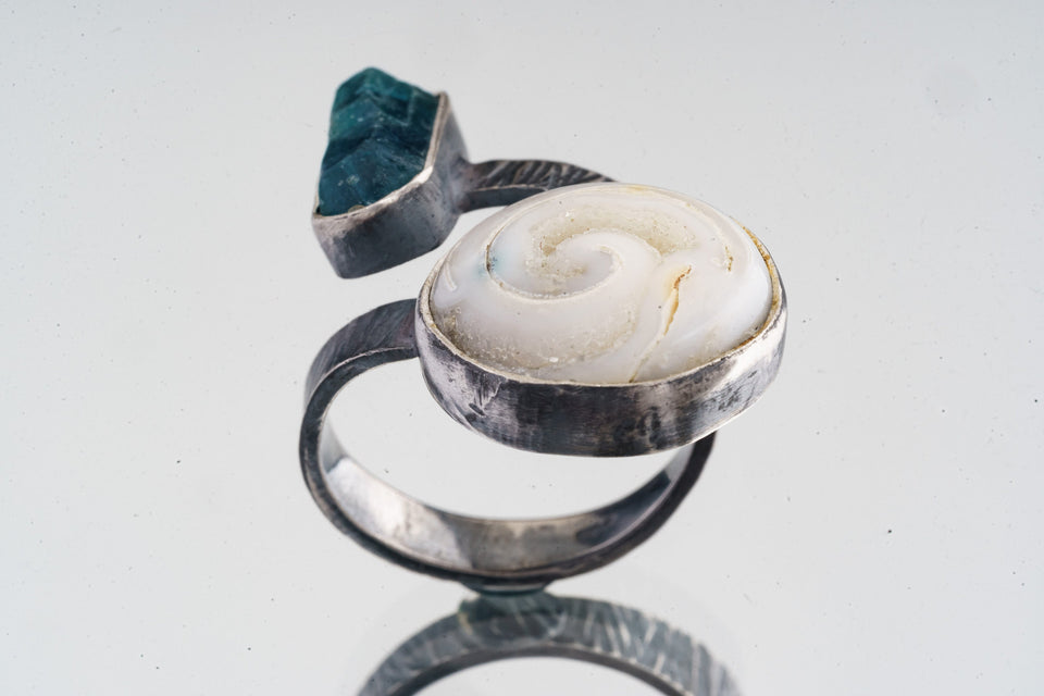 Land and Sea Apatite Shell ring shown on a white background, with blue terminated crystal and fossilized shell setting.