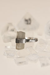 Raw Australian Aquamarine ring displayed on clear quartz, with oxidized sterling silver wrap setting and hammered band.