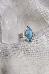 Larimar adjustable ring shown beside a quartz crystal, with high-shine sterling silver and ocean-blue eye-shaped stone.
