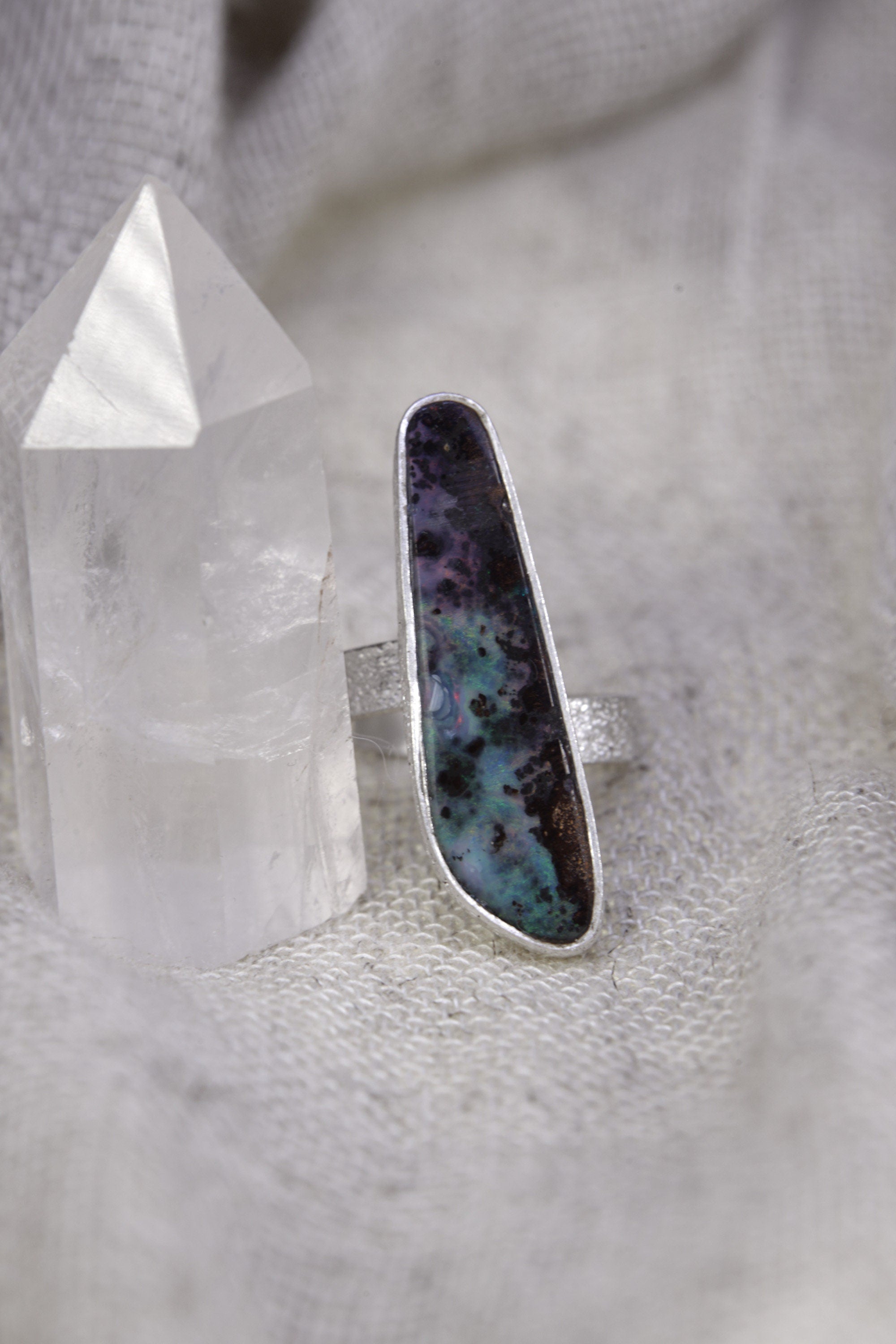 Opal sterling silver ring on soft fabric, showing the high-shine finish, textured band, and luminous blue-green colour play.