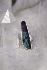 Opal sterling silver ring on soft fabric, showing the high-shine finish, textured band, and luminous blue-green colour play.