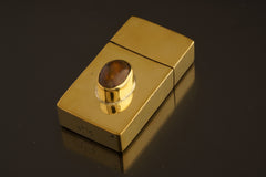 Celestial Fire brass matchbox shown on dark background with elevated Ethiopian Opal bezel and polished golden surface.