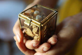 Small square brass and glass display box held in hands with jewelry and keepsakes inside.