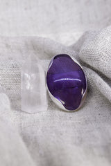 Oval Amethyst adjustable ring shown beside a quartz crystal, with waved bezel setting and textured silver band.