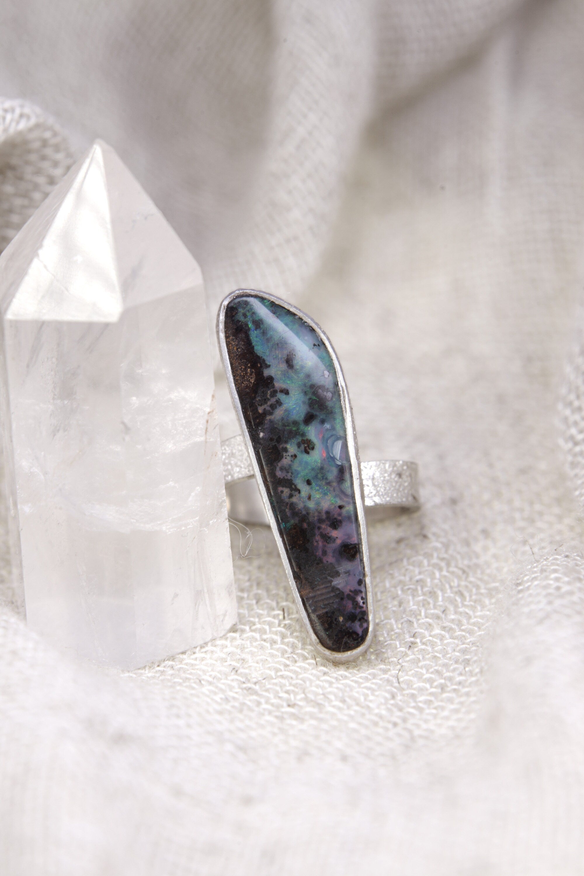 Opal adjustable silver ring shown beside a quartz crystal, with waved bezel setting and soft iridescent stone glow.