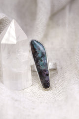 Opal adjustable silver ring shown beside a quartz crystal, with waved bezel setting and soft iridescent stone glow.