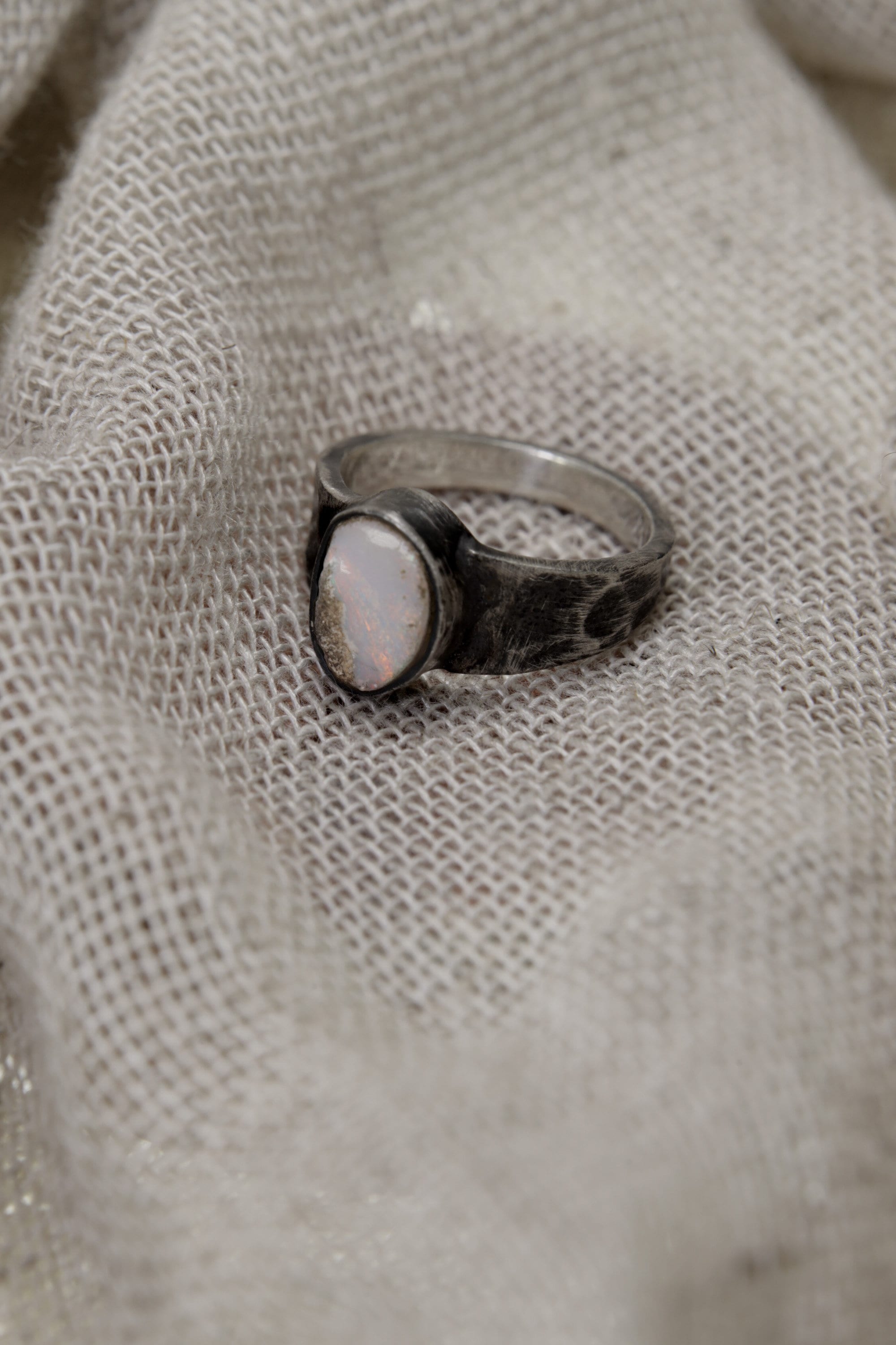 Side view of handmade Lightning Ridge Opal ring showing the raised bezel setting, textured silver band, and pale Opal face.