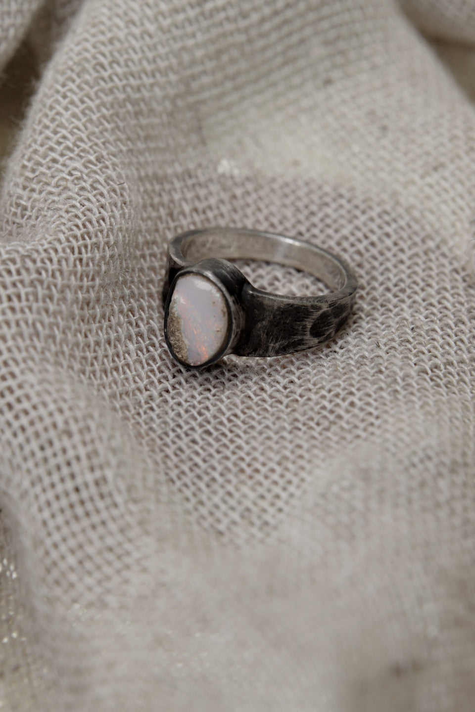 Side view of handmade Lightning Ridge Opal ring showing the raised bezel setting, textured silver band, and pale Opal face.