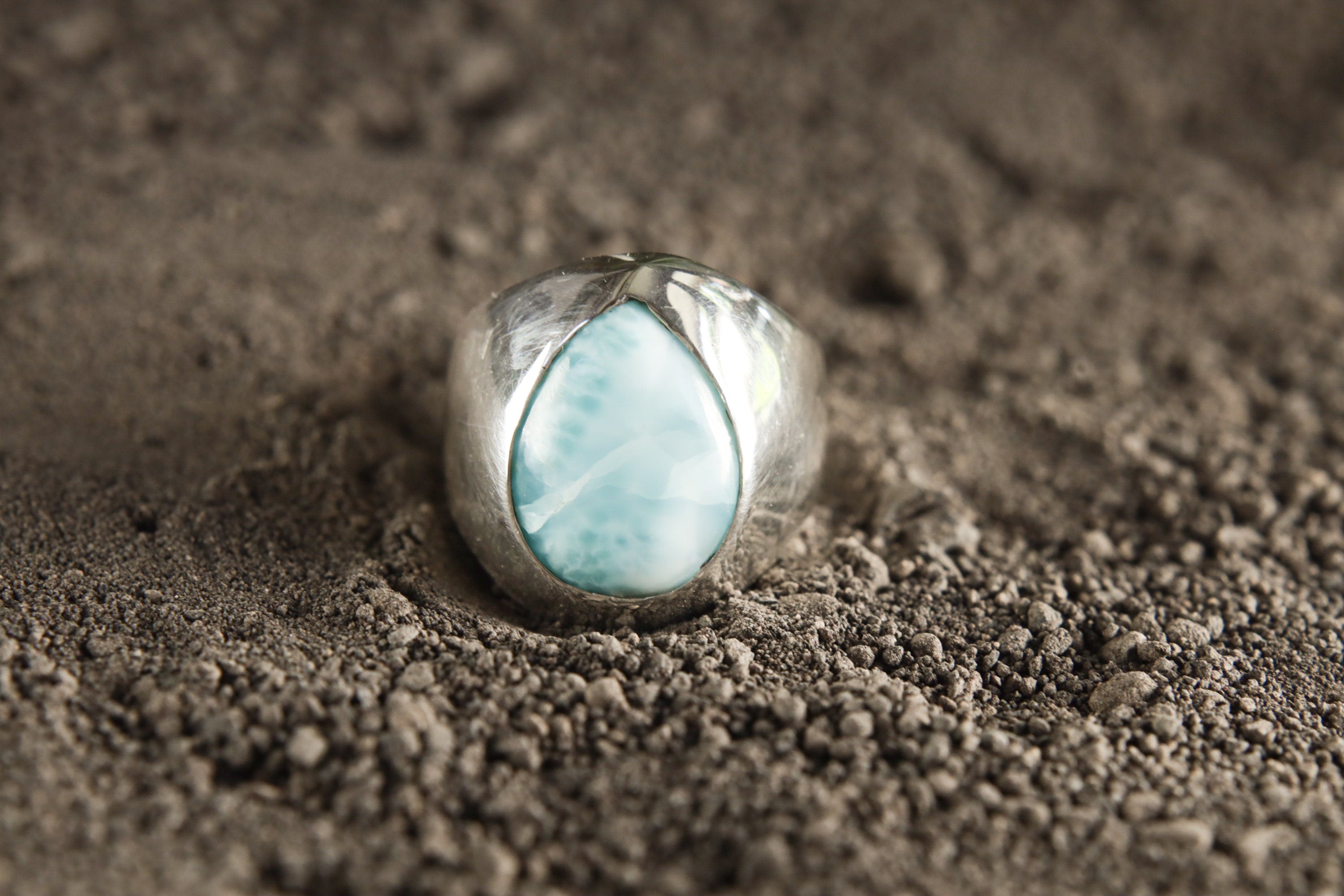 Polished 925 sterling silver Larimar cabochon ring shown on sand, with sky-blue stone and lightweight hollow statement band.
