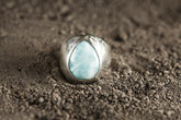 Polished 925 sterling silver Larimar cabochon ring shown on sand, with sky-blue stone and lightweight hollow statement band.