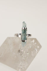 Aqua Aura Quartz ring displayed on clear quartz, showing oxidized silver band and vertical blue crystal point.