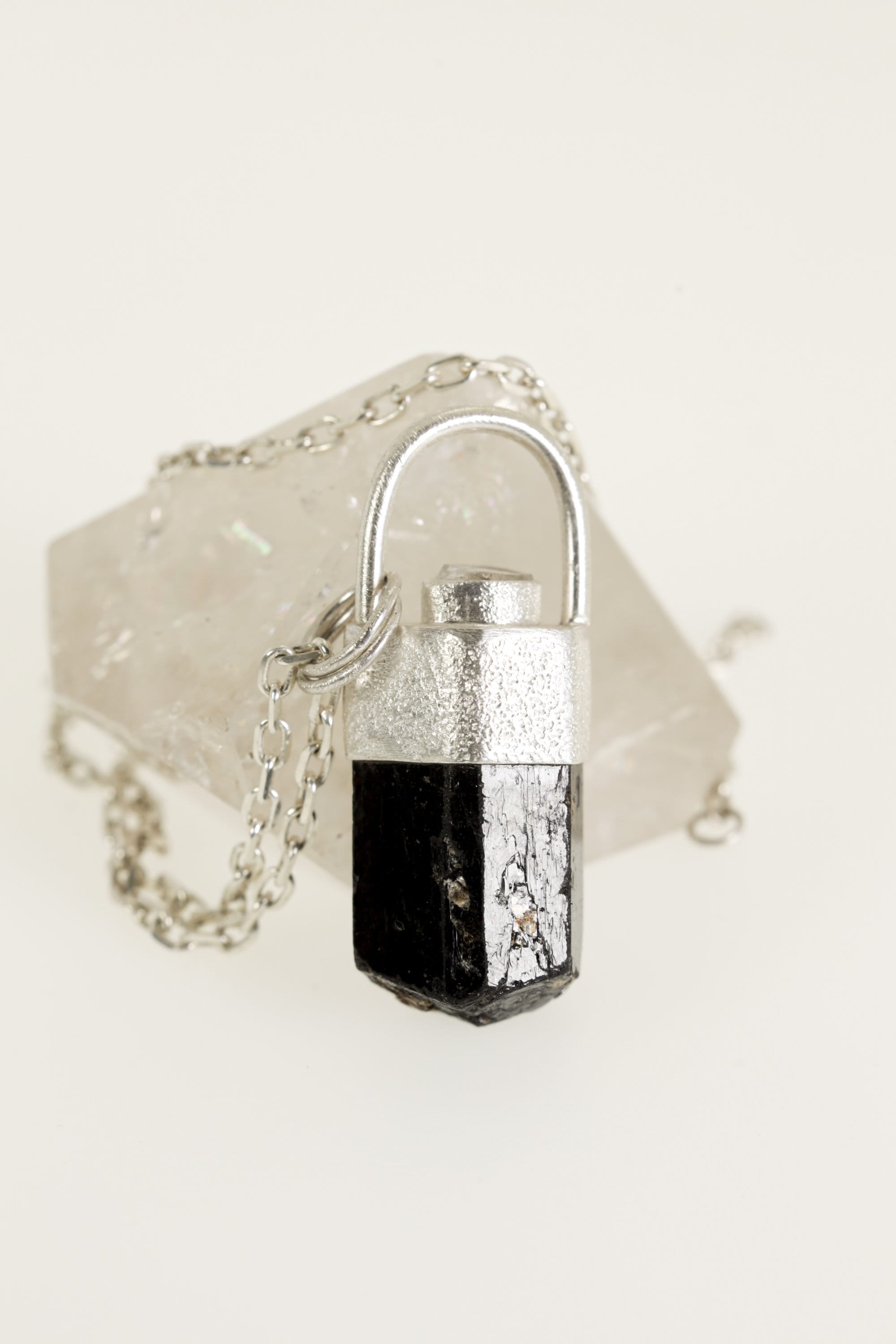 Himalayan Brown Dravite Tourmaline Diamond pendant on white background, with sand-textured sterling silver and rounded halo bail.
t is set in a silver bezel and has a faceted shape.