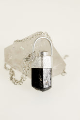 Himalayan Brown Dravite Tourmaline Diamond pendant on white background, with sand-textured sterling silver and rounded halo bail.
t is set in a silver bezel and has a faceted shape.