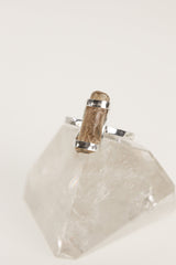 Natural Amber fossil ring displayed on clear quartz, with polished sterling silver band and warm golden organic gemstone.