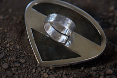 Teardrop Labradorite ring shown on earthy background, with waved bezel setting and shifting aurora-like colour flash.