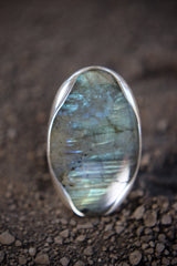 Close-up of oval Labradorite in a high-shine sterling silver ring, showing aurora-like flash and textured band detail.