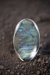 Close-up of oval Labradorite in a high-shine sterling silver ring, showing aurora-like flash and textured band detail.