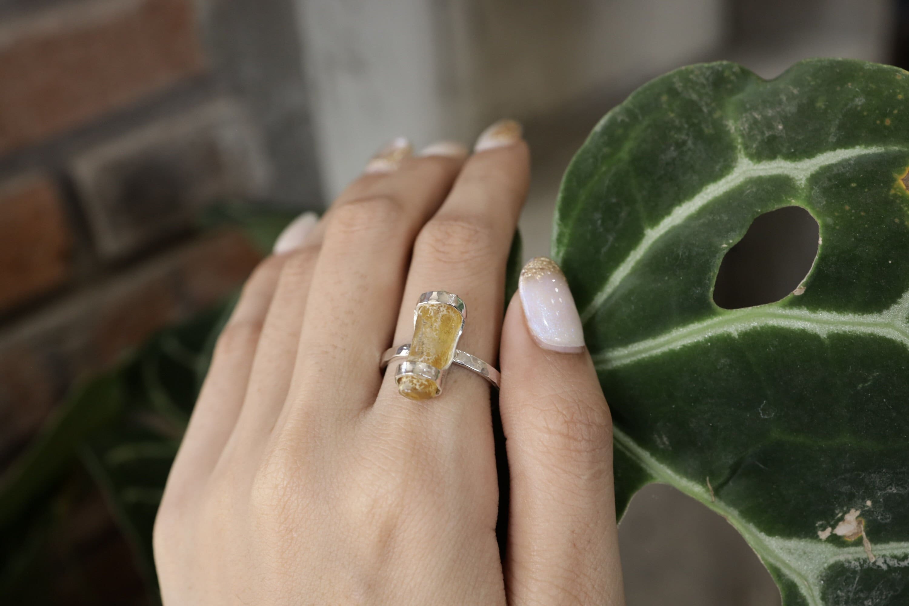 Handmade 925 sterling silver Amber fossil ring shown worn on the hand, with warm honey-gold stone and textured silver band.