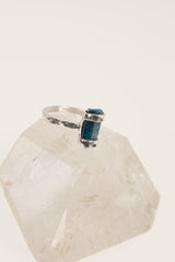 Blue Apatite ring displayed on clear quartz, showing oxidized silver band and vertical terminated blue crystal.