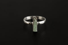 Aquamarine silver ring shown on a dark background, featuring long vertical blue gemstone and polished hammered band.