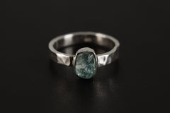 Raw Blue Apatite Gem Ring shown on black background with hammered sterling silver band and raw blue-green gemstone.