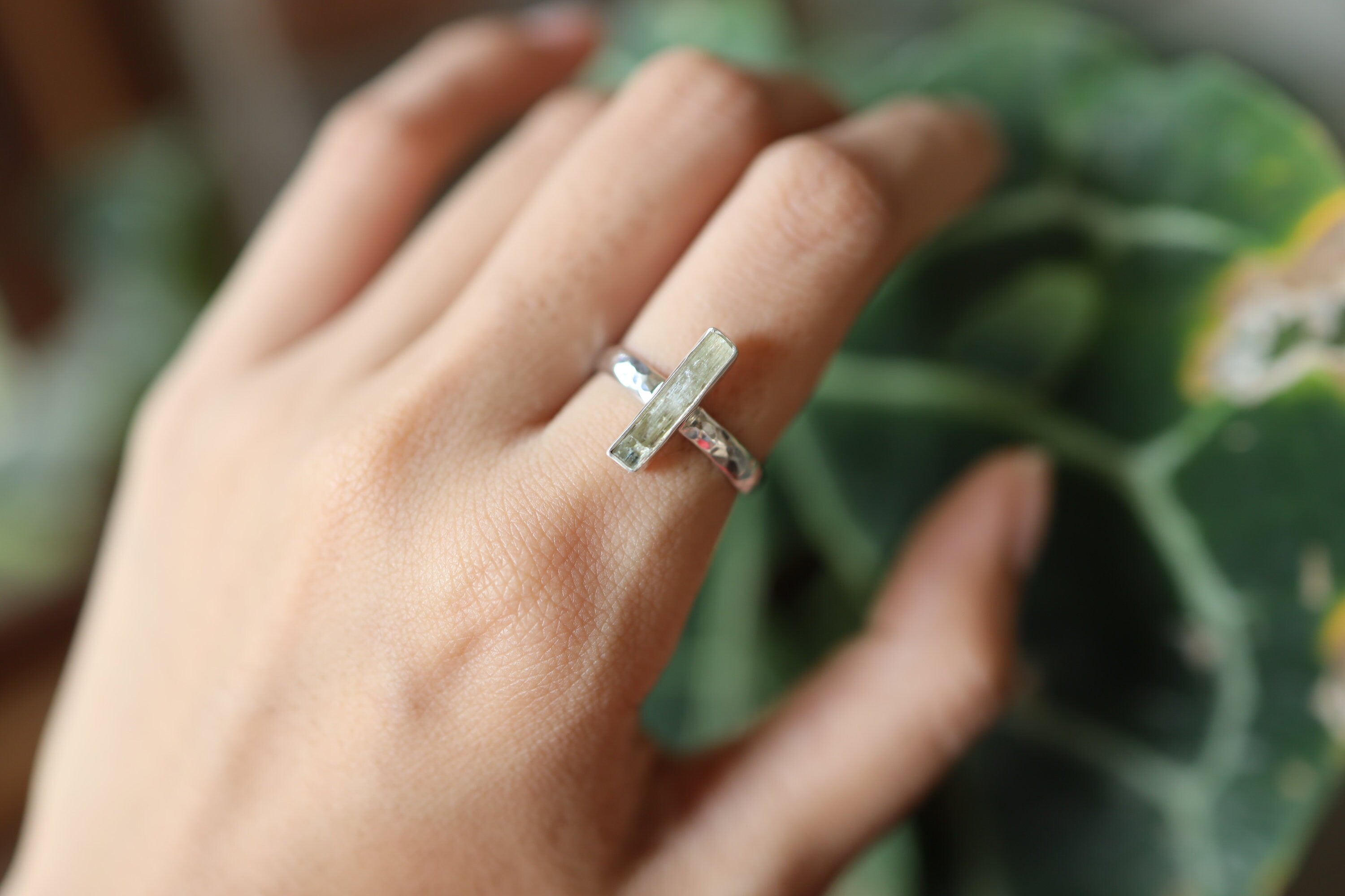 Long square cut Aquamarine silver ring shown worn on a hand, with polished hammered sterling silver and blue gemstone.