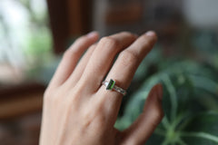 Green Tourmaline ring shown worn on a hand against leaves, with polished silver and deep green crystal detail.