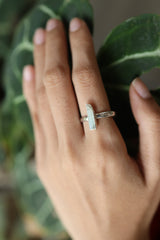 Long Aquamarine sterling silver ring shown worn on a hand, with polished hammered band and pale blue gemstone.