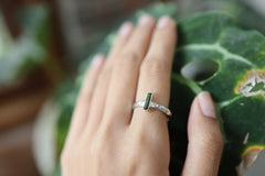 Green Tourmaline ring shown worn on a hand against leaves, with polished silver and deep green crystal detail.