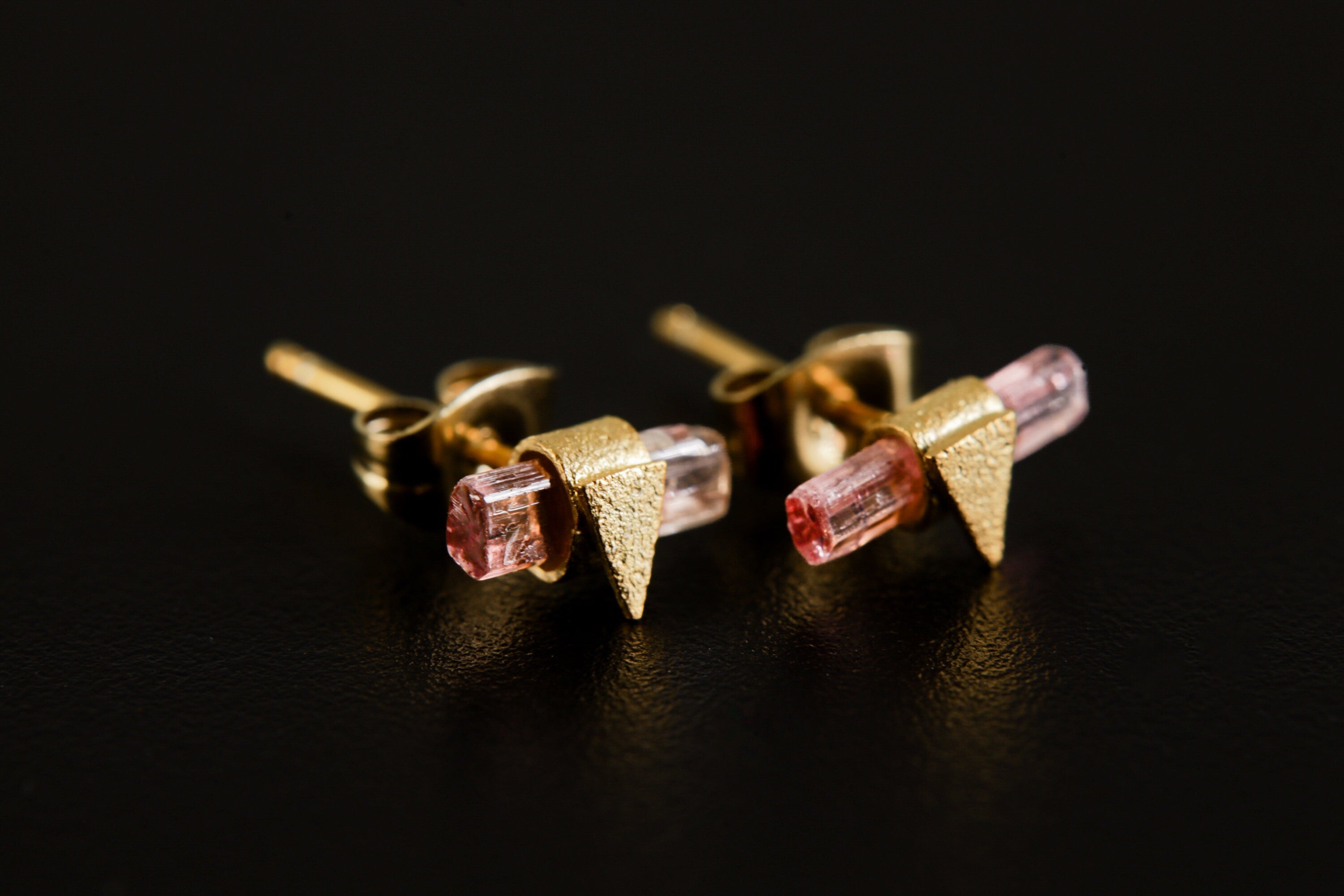 Handmade gold-plated 925 sterling silver Pink Tourmaline triangle stud earrings shown on a dark background, with raw pink crystals.