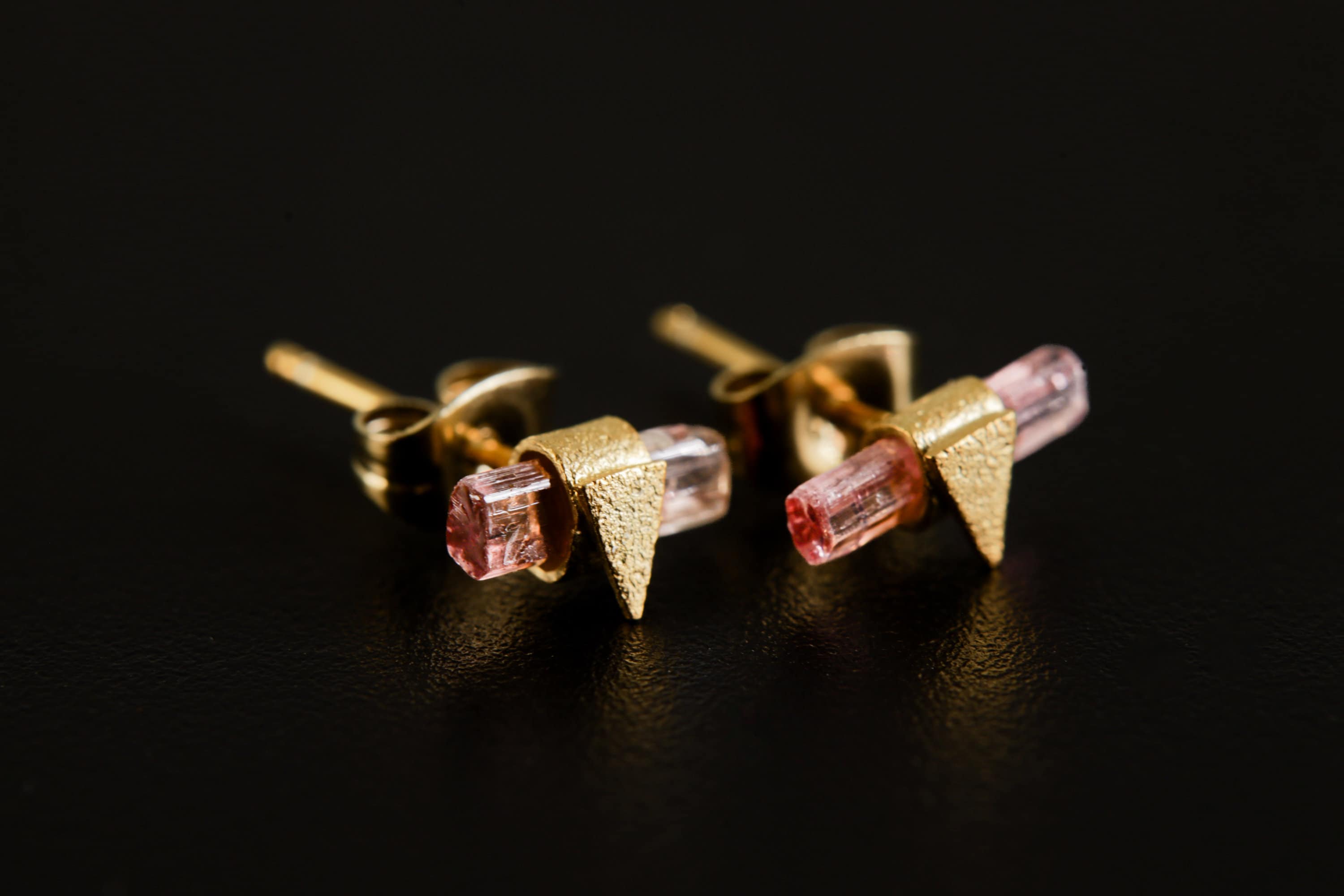 Handmade gold-plated 925 sterling silver Pink Tourmaline triangle stud earrings shown on a dark background, with raw pink crystals.
