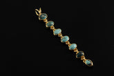 Long seven-stone Turquoise cascade pendant in 18k gold-plated sterling silver, shown on a dark background.